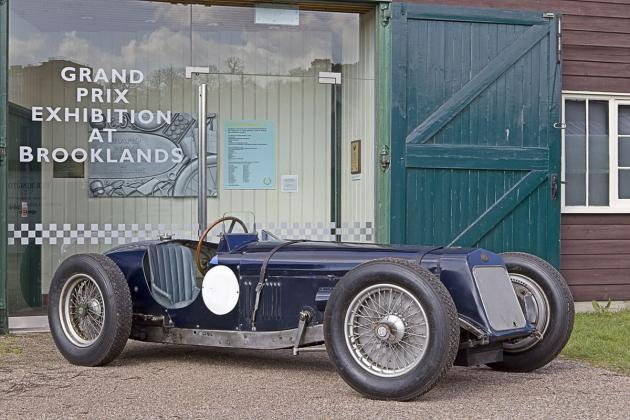 Vintage blue open-wheel racing car parked in front of the Grand Prix Exhibition at Brooklands Museum.
