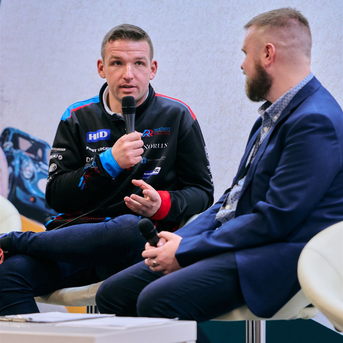 BTCC driver Chris Smiley in a Restart Racing team jacket speaking to a live audience at an event.