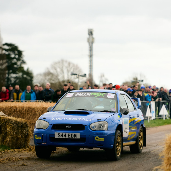 Blue Subaru Impreza WRX rally car with license plate S44 EDM competing at a rally stage with spectators.