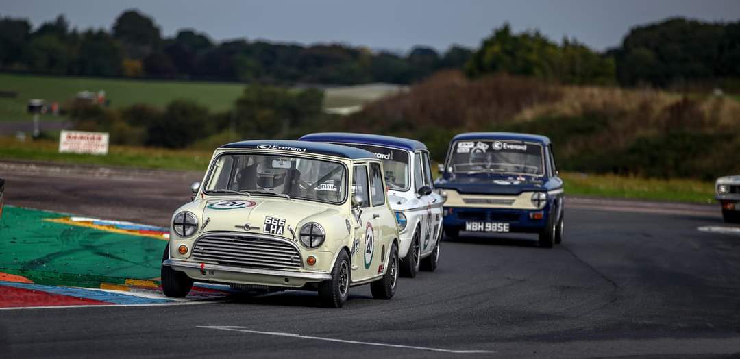 Classic Mini Cooper S race cars competing in a vintage touring car championship on a professional race track.