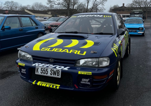 Classic blue Subaru Impreza WRX rally car with Repsol and Pirelli logos on display with other vintage cars, including a Lancia Delta.