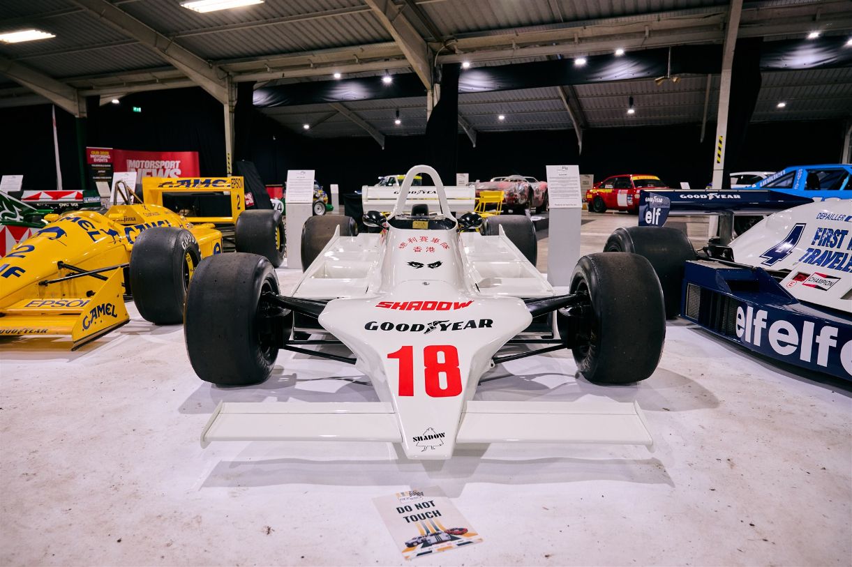 White Shadow DN9 F1 car with Goodyear branding and number 18, displayed at a motorsport exhibition with other vintage race cars.