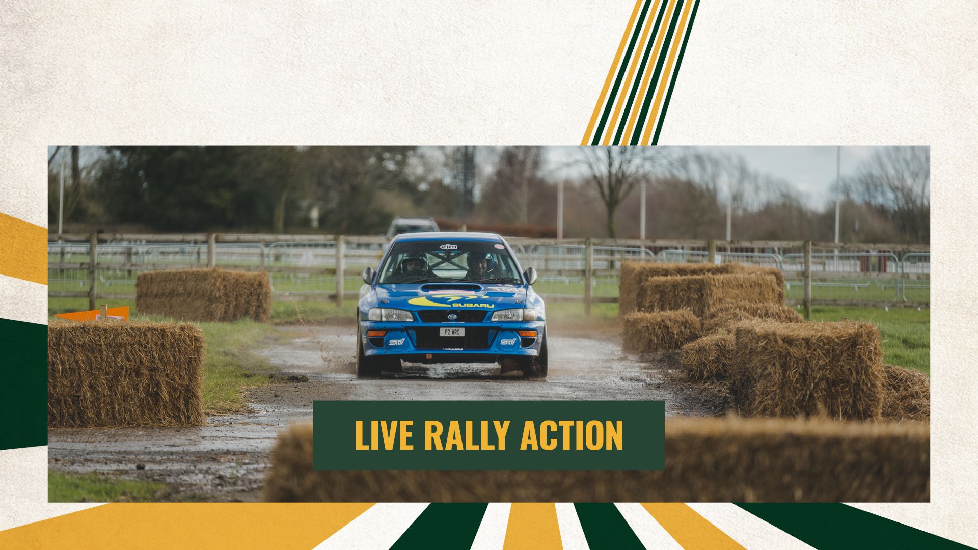 A blue Subaru Impreza rally car driving through a dirt and mud course with hay bales at a live motorsport event.