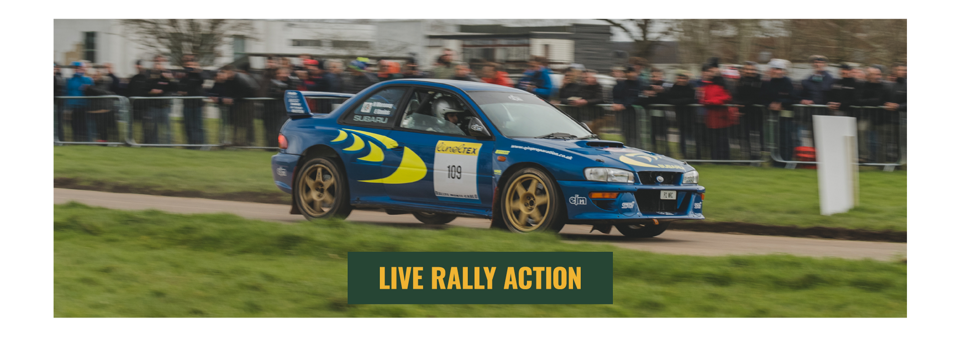 Blue Subaru Impreza rally car driving at speed during a live rally action demonstration at a motorsport show.