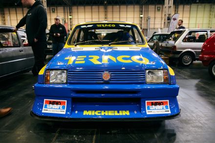 Blue and yellow MG Metro rally car with Texaco livery on display at an indoor classic car show.