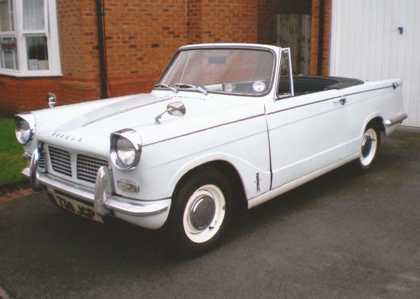Classic white Triumph Herald convertible parked on a residential driveway.