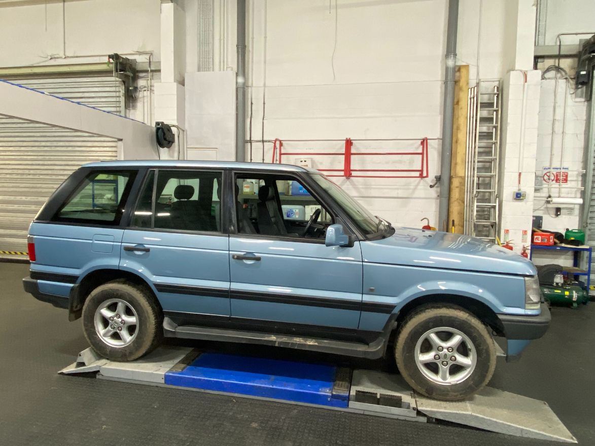 Light blue Range Rover P38 SUV parked on a vehicle lift inside a workshop.