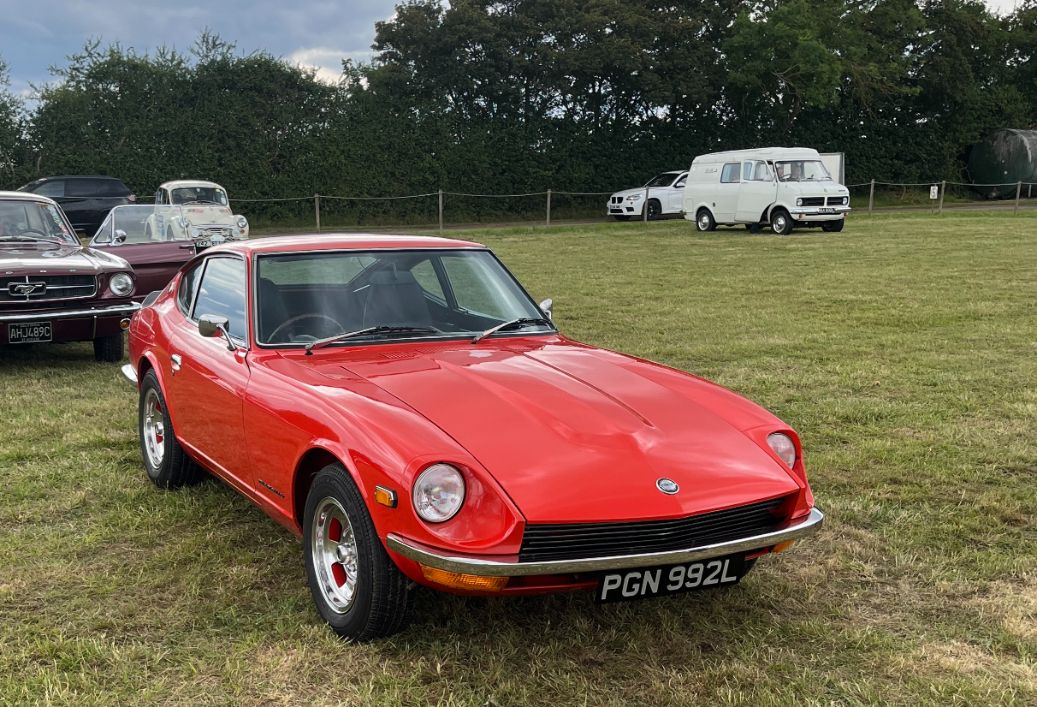 Bright red Datsun 240Z sports car parked on grass at an outdoor classic car meet.