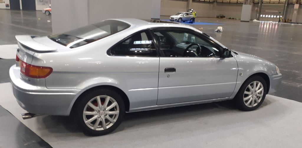 Silver Toyota Paseo coupe with rear spoiler displayed on a showroom floor.