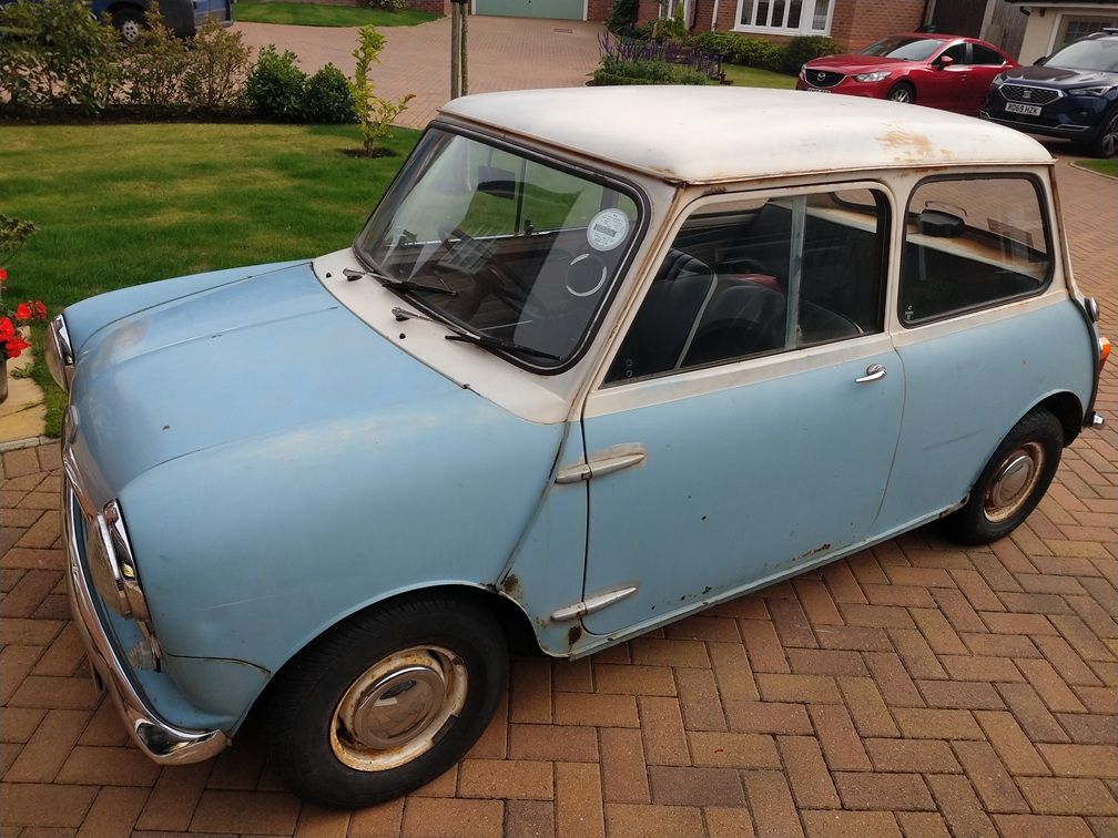 Two-tone blue and white classic Austin Mini barn find with surface rust parked on a brick driveway.