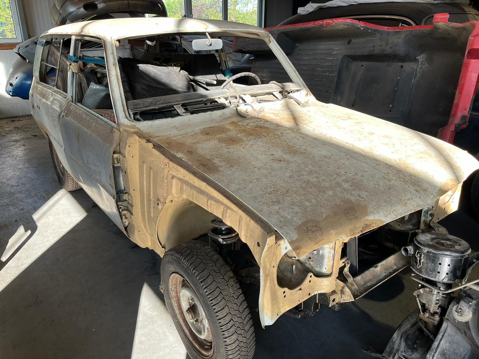 Rare white Mazda 120Y Estate project car with significant rust and missing front panels in a garage.