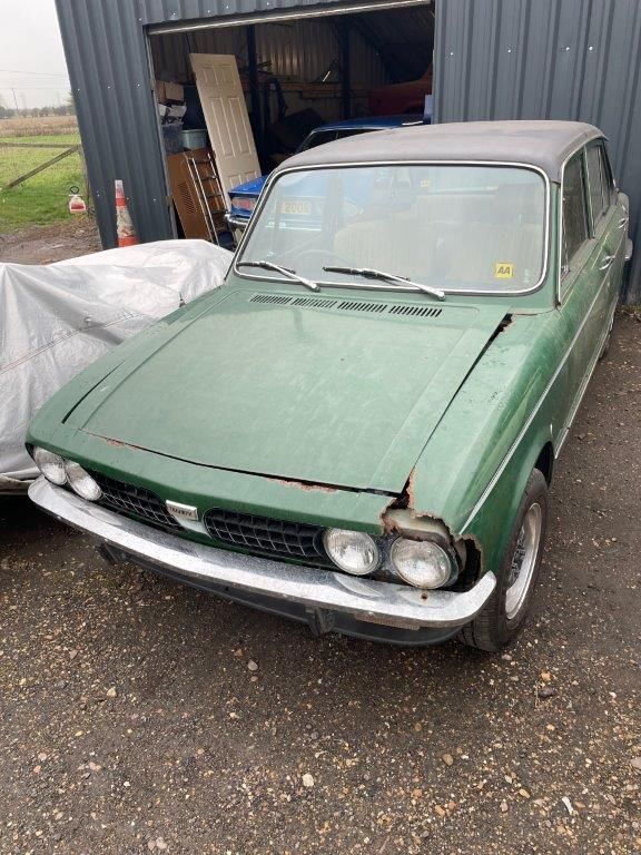 Green Triumph Dolomite project car with front-end rust damage parked outside a metal workshop.