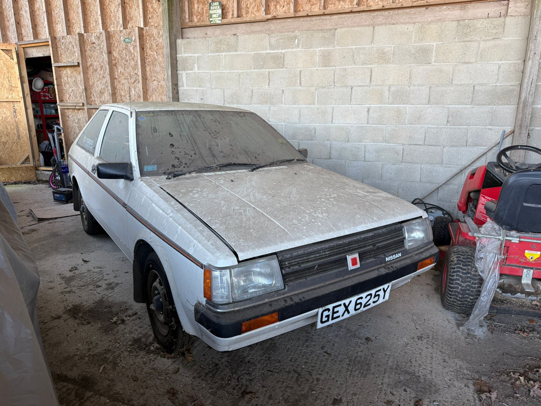 Red Datsun Cherry N10 project car with visible rust and "barn find" patina in a garage.
