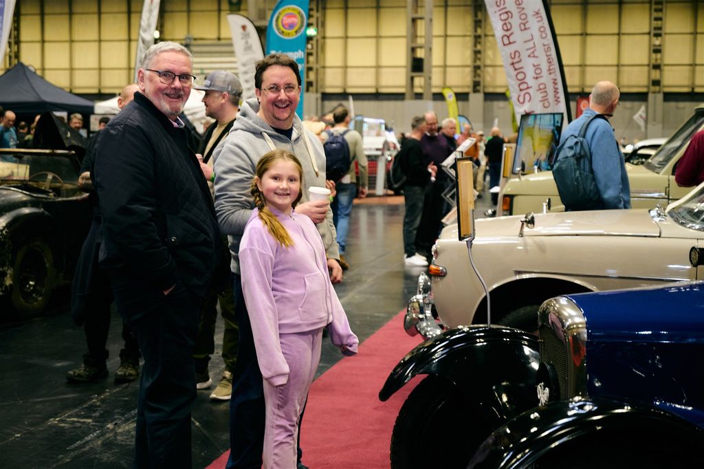 Families and classic car enthusiasts attending an indoor automotive exhibition featuring vintage cars on display.