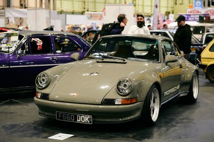 Custom Porsche 911 restomod in Nardo Gray with widebody kit and vintage decals at a classic car show.