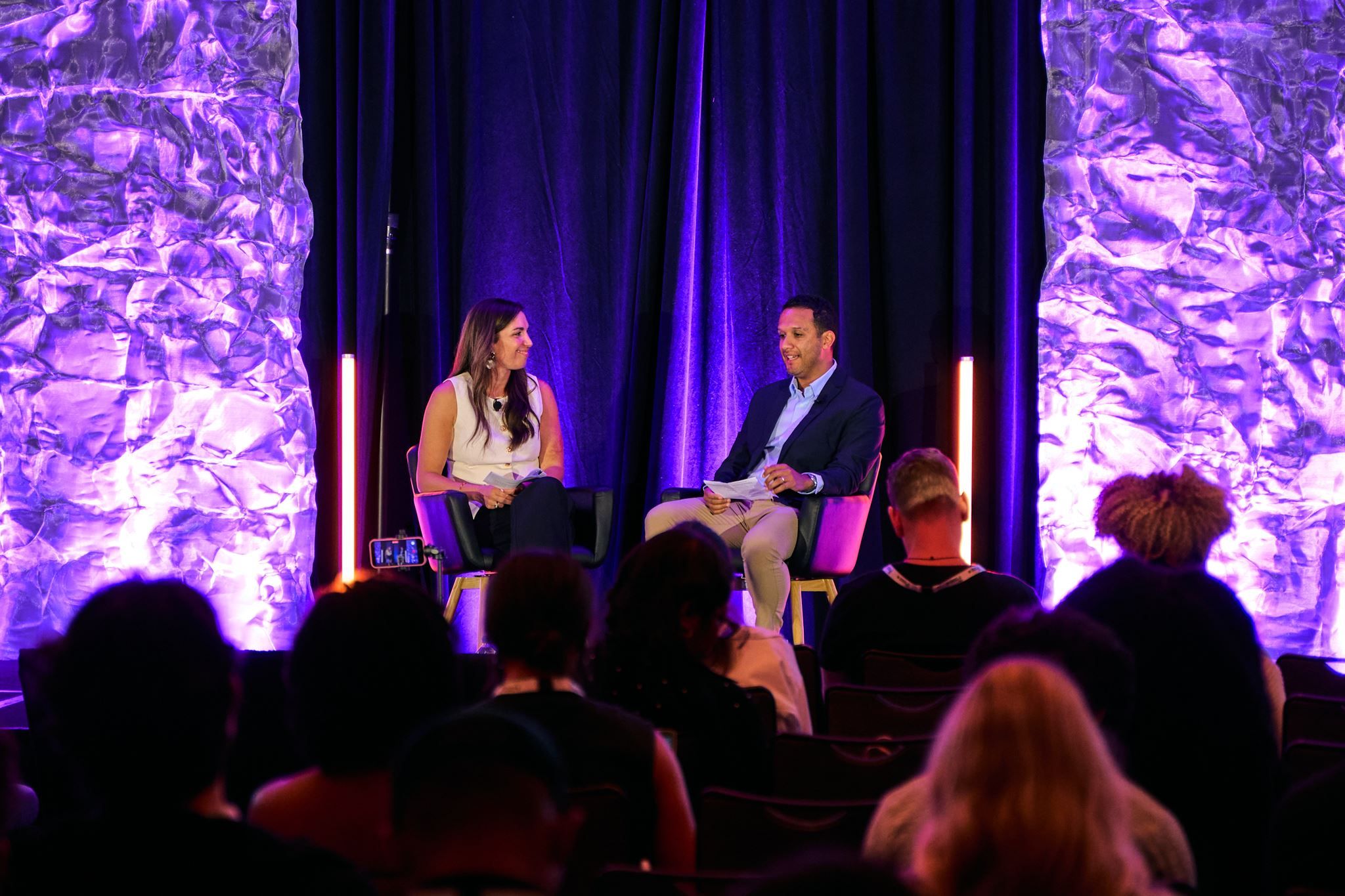 Two Creator Economy Live West speakers in conversation on a purple-lit conference stage, with audience members silhouetted in the foreground.