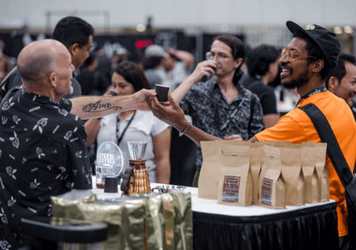 Exhibitor and attendee smiling while exhibitor hands sample of coffee over
