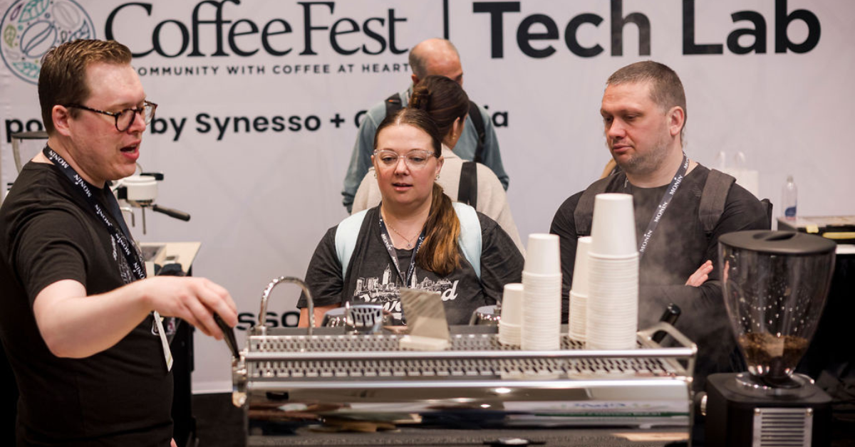 Attendees in front of an espresso machine learning from a Synesso Middleby technician