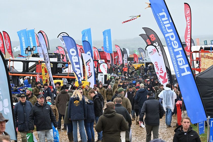 A group of young men walking through an outdoor event or fair, surrounded by tents and equipment displays.
