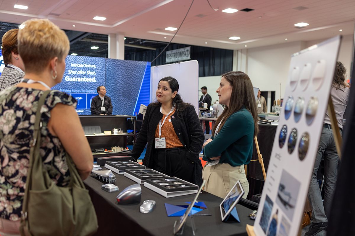Photo shows visitors of Automotive Interiors Expo North America speaking to an exhibitor