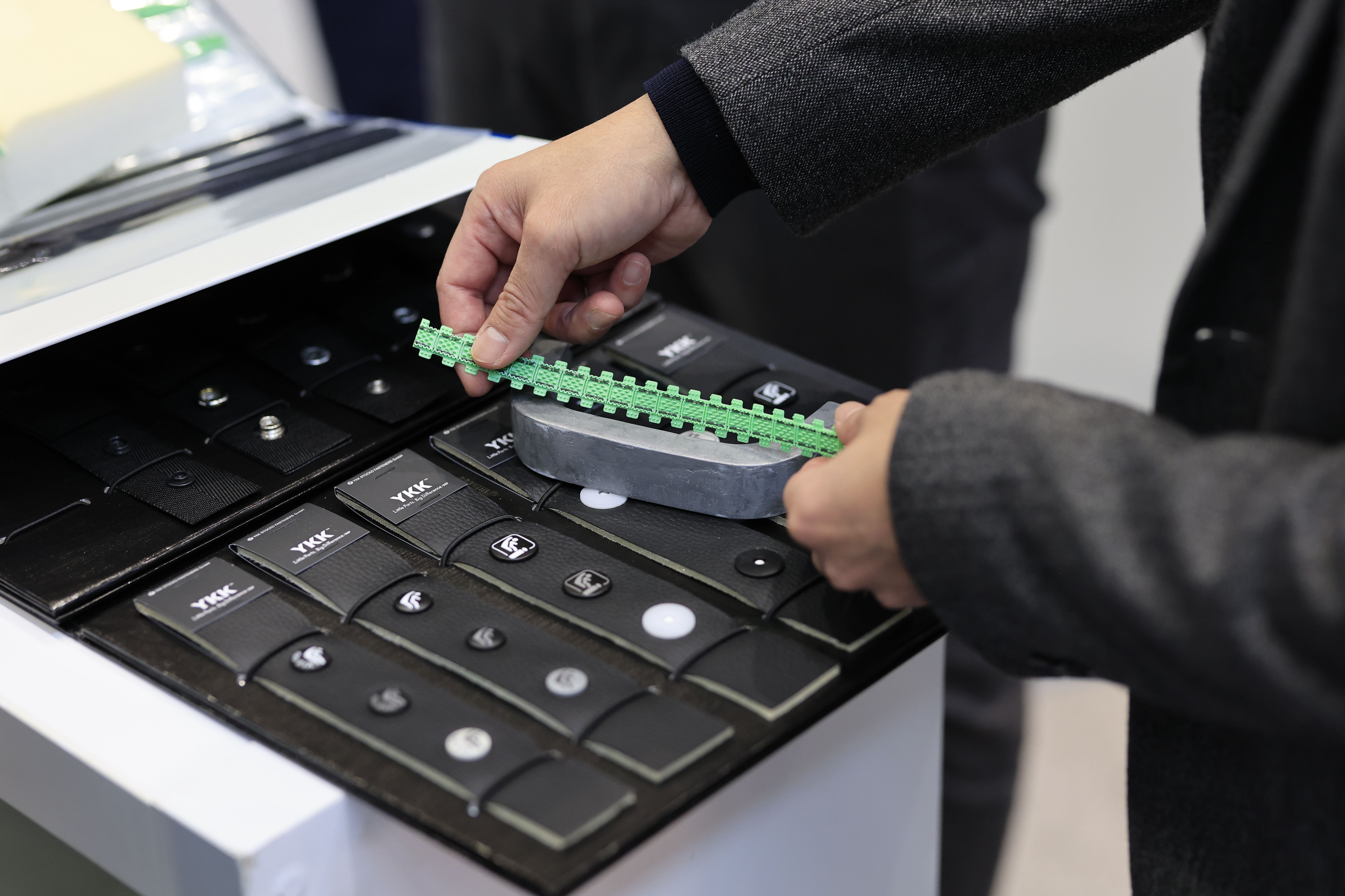Photo shows a visitor at Automotive Interiors Expo North America measuring a piece of material