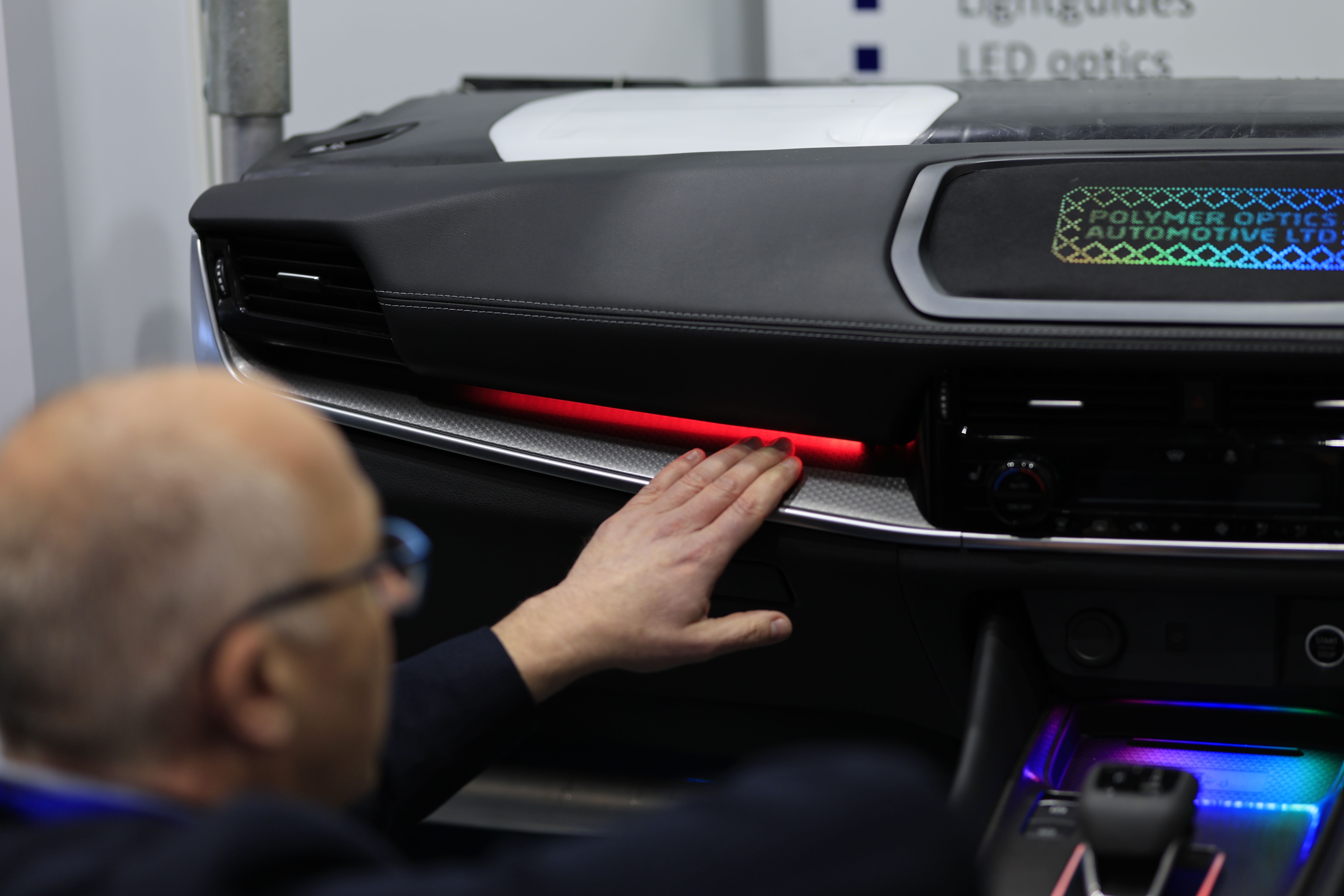 Photo shows a visitor at Automotive Interiors Expo North America exploring the dashboard of a car