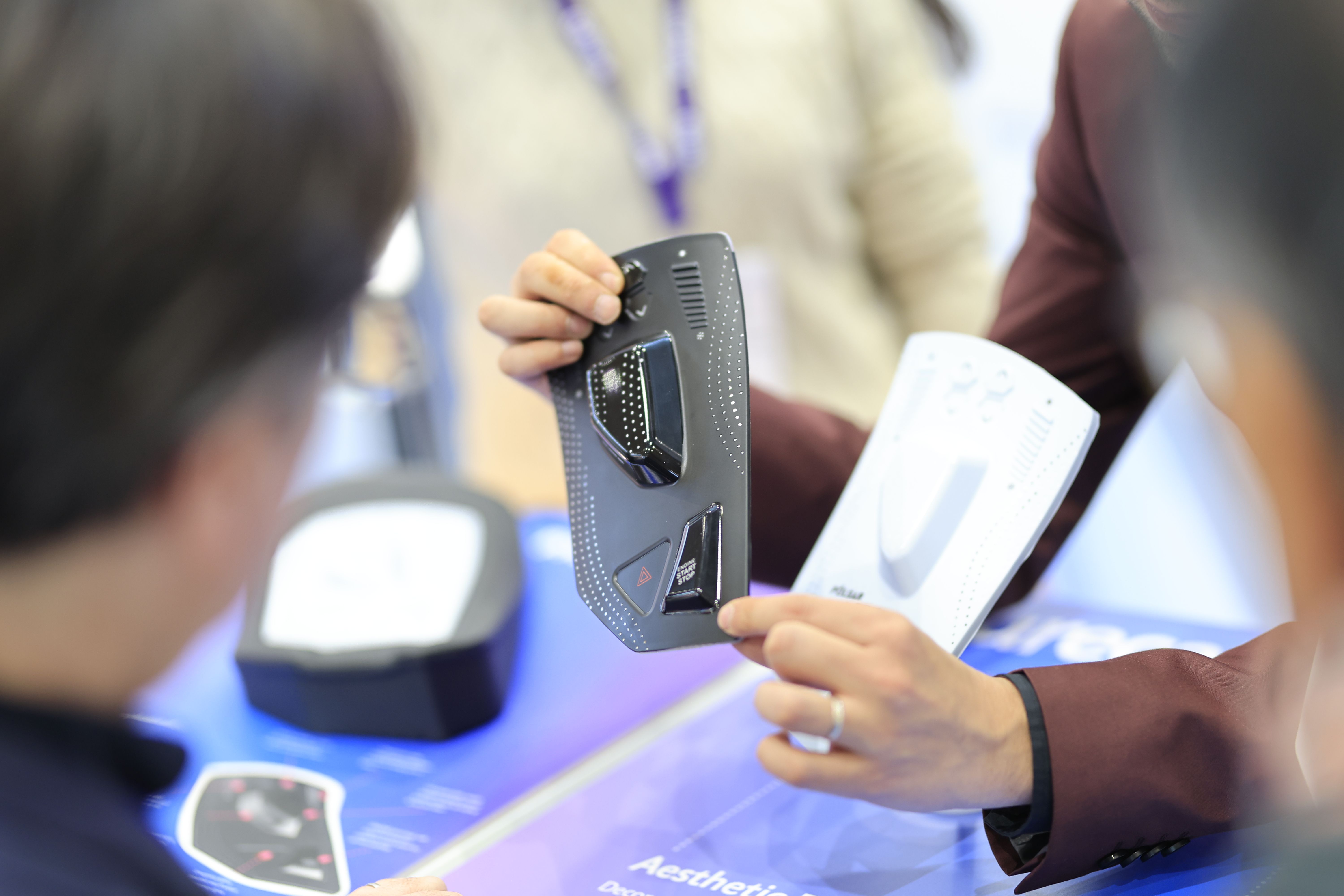 Photo shows an exhibitor explaining a piece of technology they are displaying at Automotive Interiors Expo North America