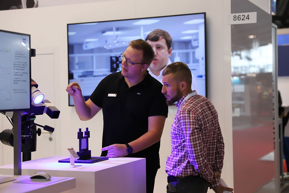 Photo shows an exhibitor at Automotive Testing Expo engaged in conversation with a visitor