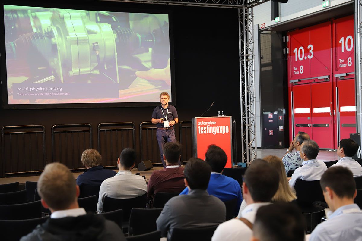 Photo shows a man speaking to an engaged audience on stage at the Automotive Testing Expo in Stuttgart, Germany