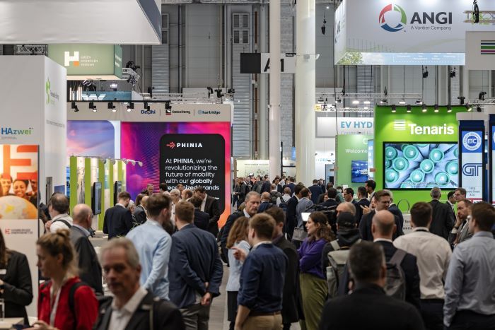 A busy exhibition hall filled with people walking, talking, and visiting various company stands with colourful displays and signage in a modern, well-lit venue. related image