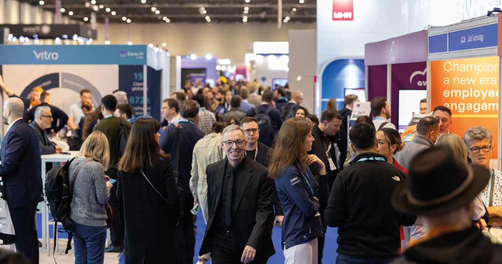 A busy aisle at HR Technologies UK 2024, with a smiling attendee in the centre