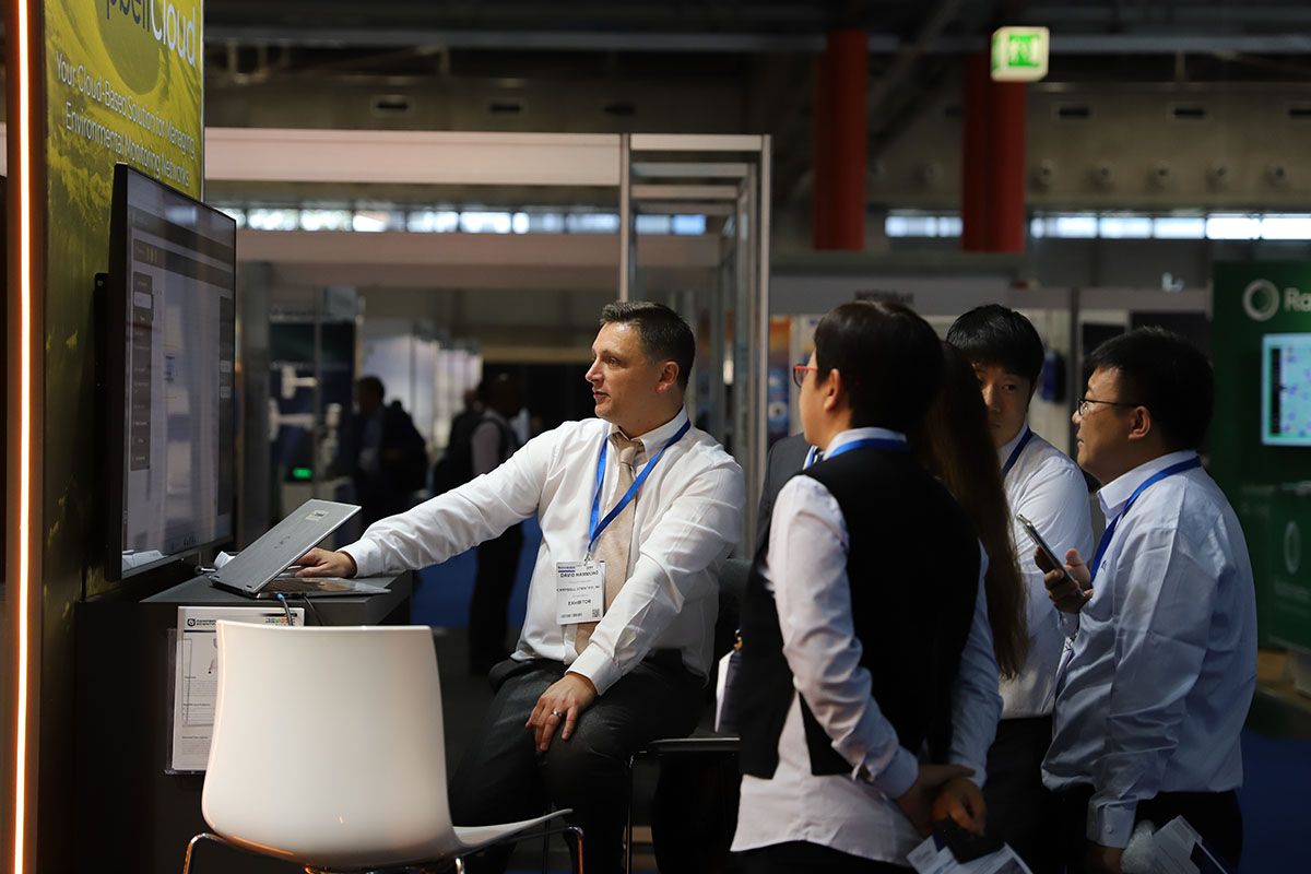 Photo shows an exhibitor talking through the software they are showcasing to a group of engaged visitors