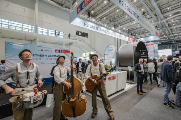 3 Men dressed in matching brown outfits each playing a different instrument on the expo floor