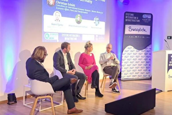 Four panelists seated on stage discuss the Green Hydrogen Hub in Northern Germany, with a presentation screen and branded sponsor signage in the background.