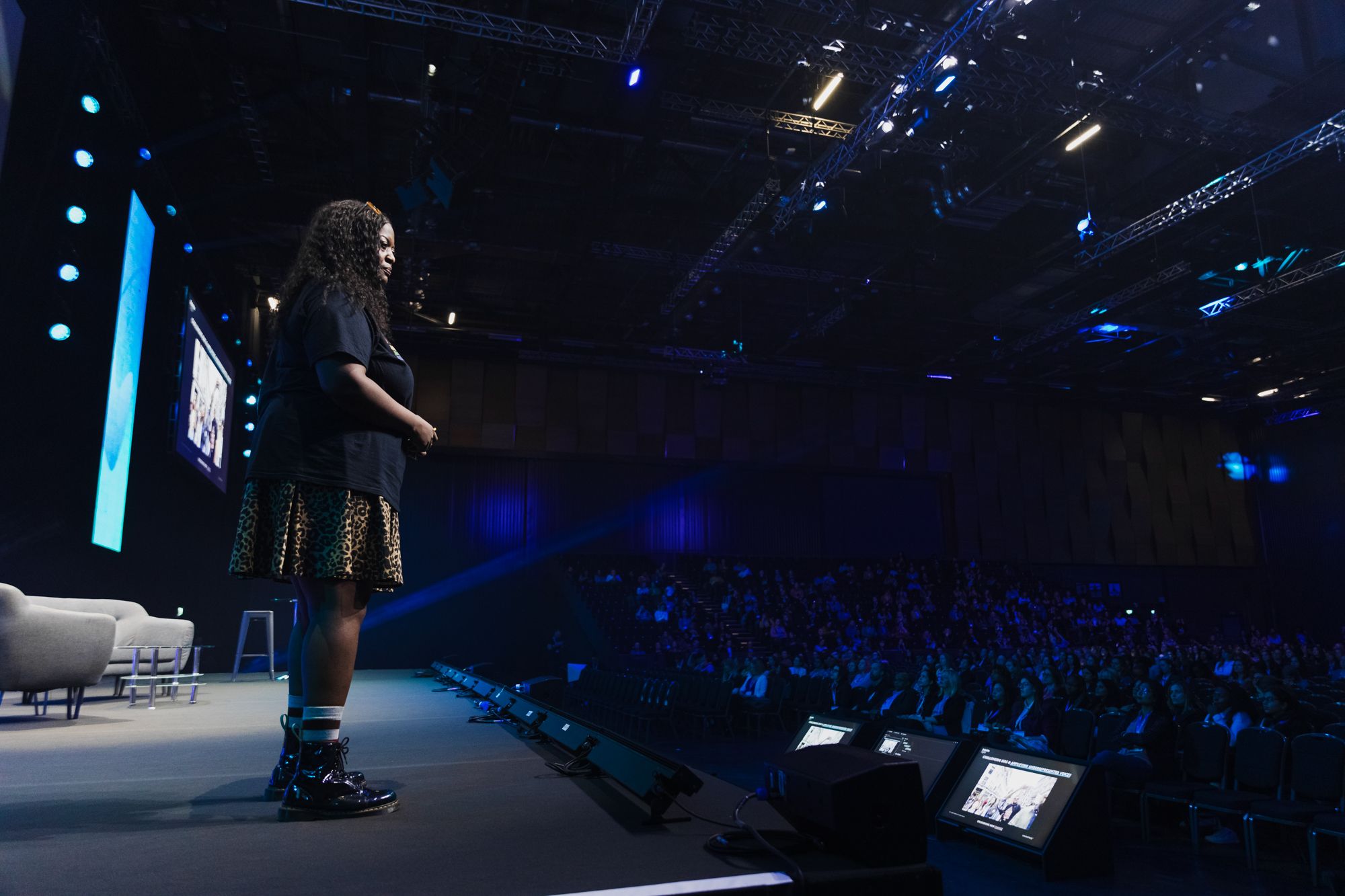 Image of a woman stood on stage delivering a presentation to a large audience