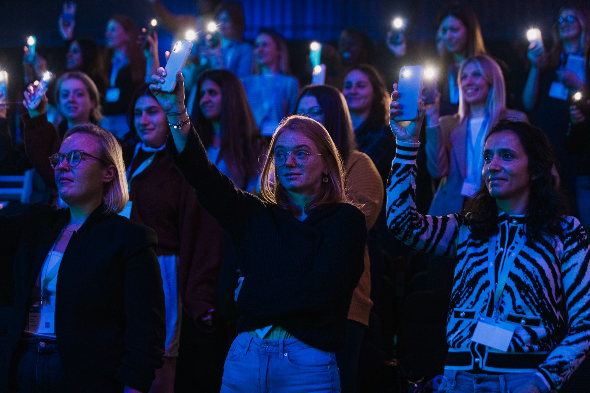 Image of an audience of women holding their camera torches high in the air