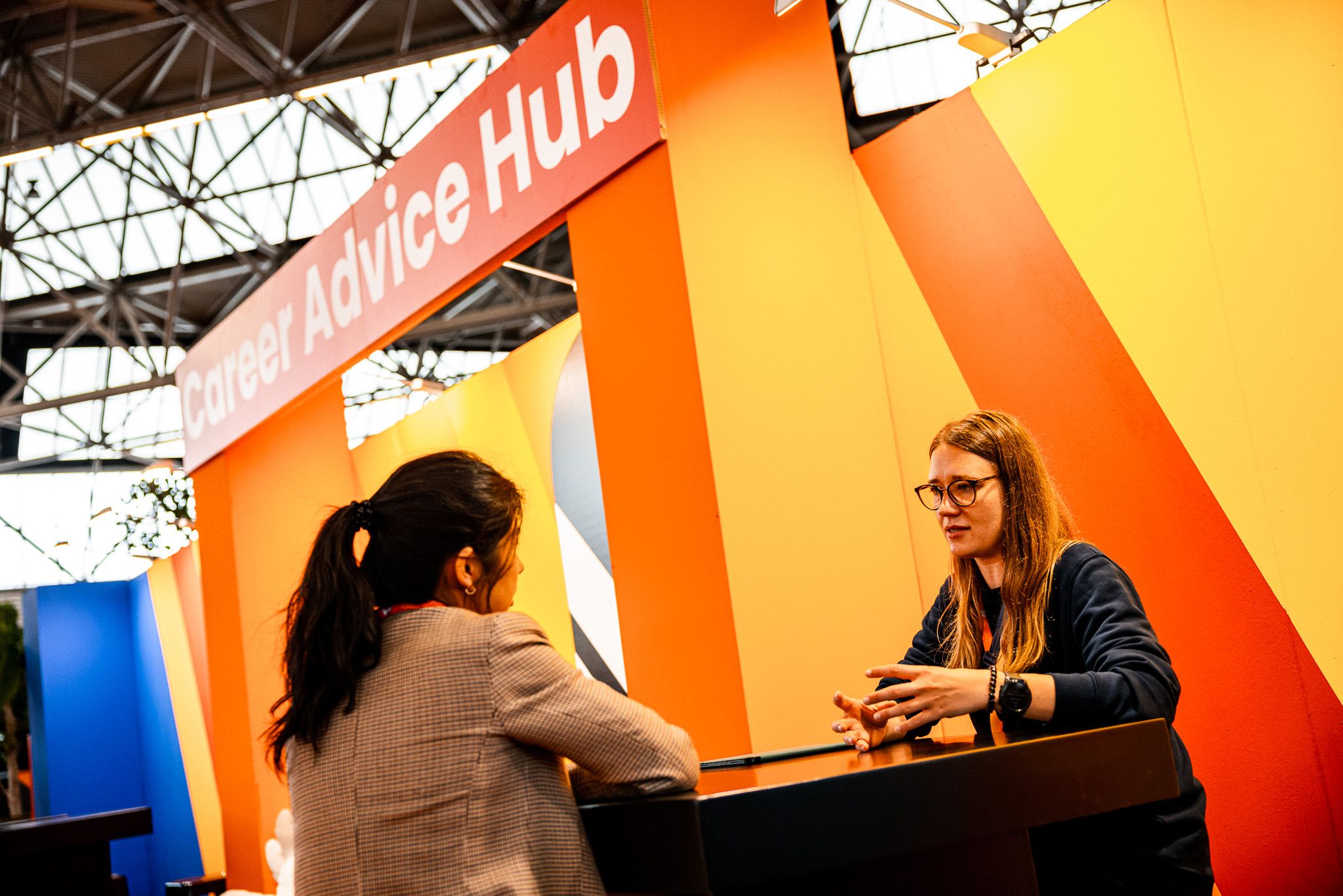 Image of two women sat opposite each other on a table conversing under a sign that reads Career Advice Hub