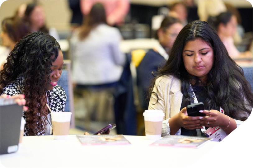 2 women sat at table working networking on their phones