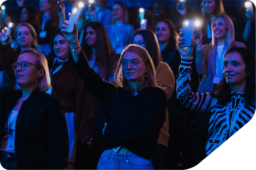Image of an audience of women holding their camera torches high in the air