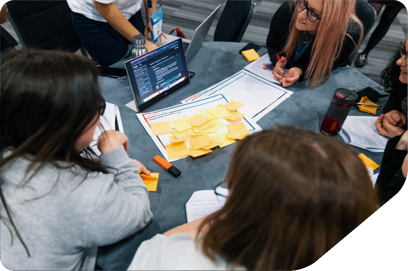 women sat around table with laptop, tables and workshop sheets problem solving