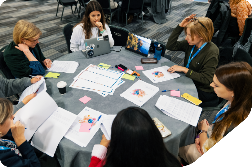 women sat around table with laptop, tables and workshop sheets problem solving