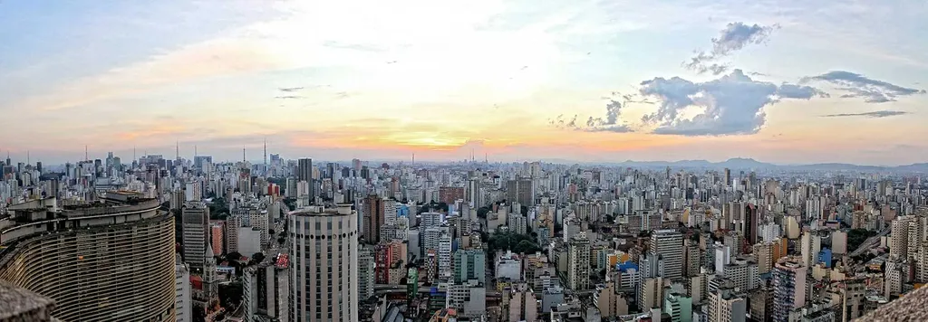 A sweeping panoramic view of the dense S&atilde;o Paulo, Brazil skyline filled with countless high-rise buildings and skyscrapers under a soft sunset sky.