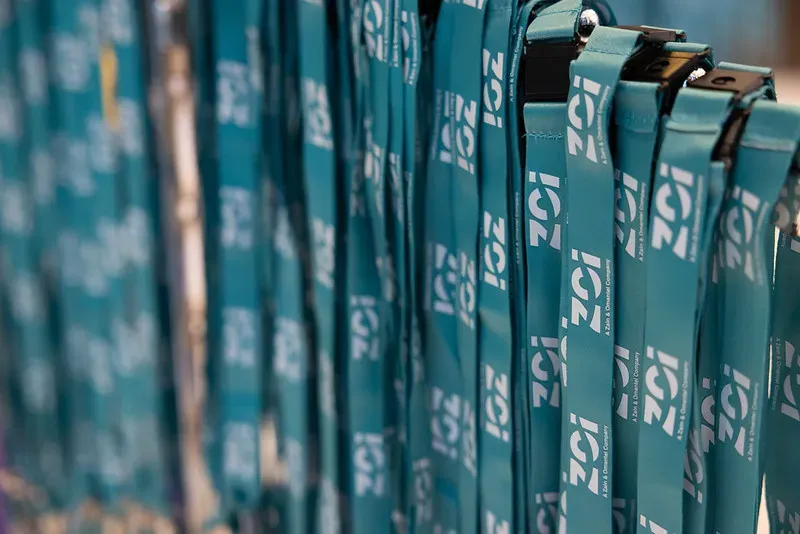 A tight macro shot of a dense row of matching teal event lanyards hanging ready for attendees, each printed repeatedly with the white 