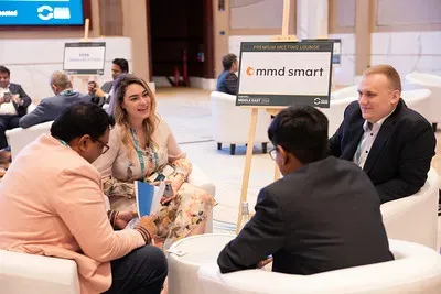 A group of four professionals seated in modern, low-profile white leather armchairs, conversing inside an open lounge area. A nearby sign on a wooden easel reads 