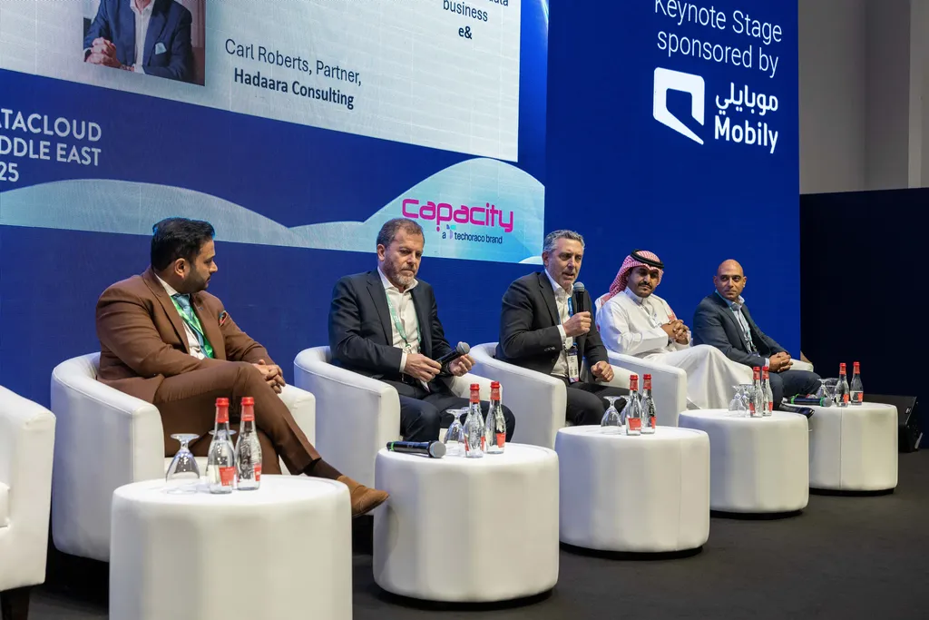 A five-person panel discussion on a stage branded 