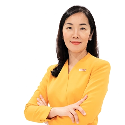 A portrait of Ubonpan Chuencom with dark hair wearing a bright yellow blazer against a clean white background, with her arms crossed.