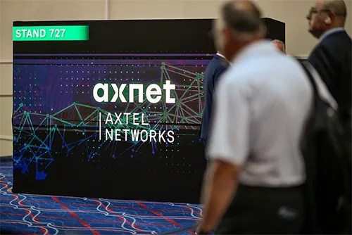 A medium shot of a digital exhibition display screen on a carpeted conference floor. The black screen features the white logo 