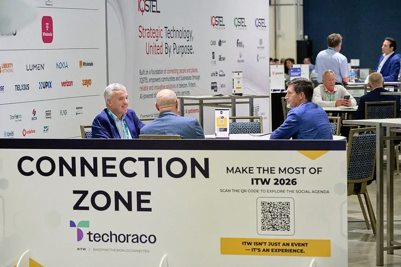 A wide, eye-level shot of a networking area at a professional event. In the foreground, a large white sign reads 