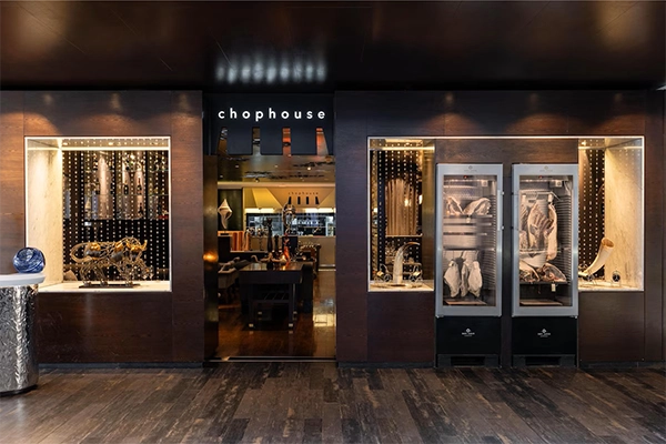 Exterior entrance of Chophouse restaurant featuring dark wood paneling, dry-aging meat display cabinets, and decorative bull sculptures.