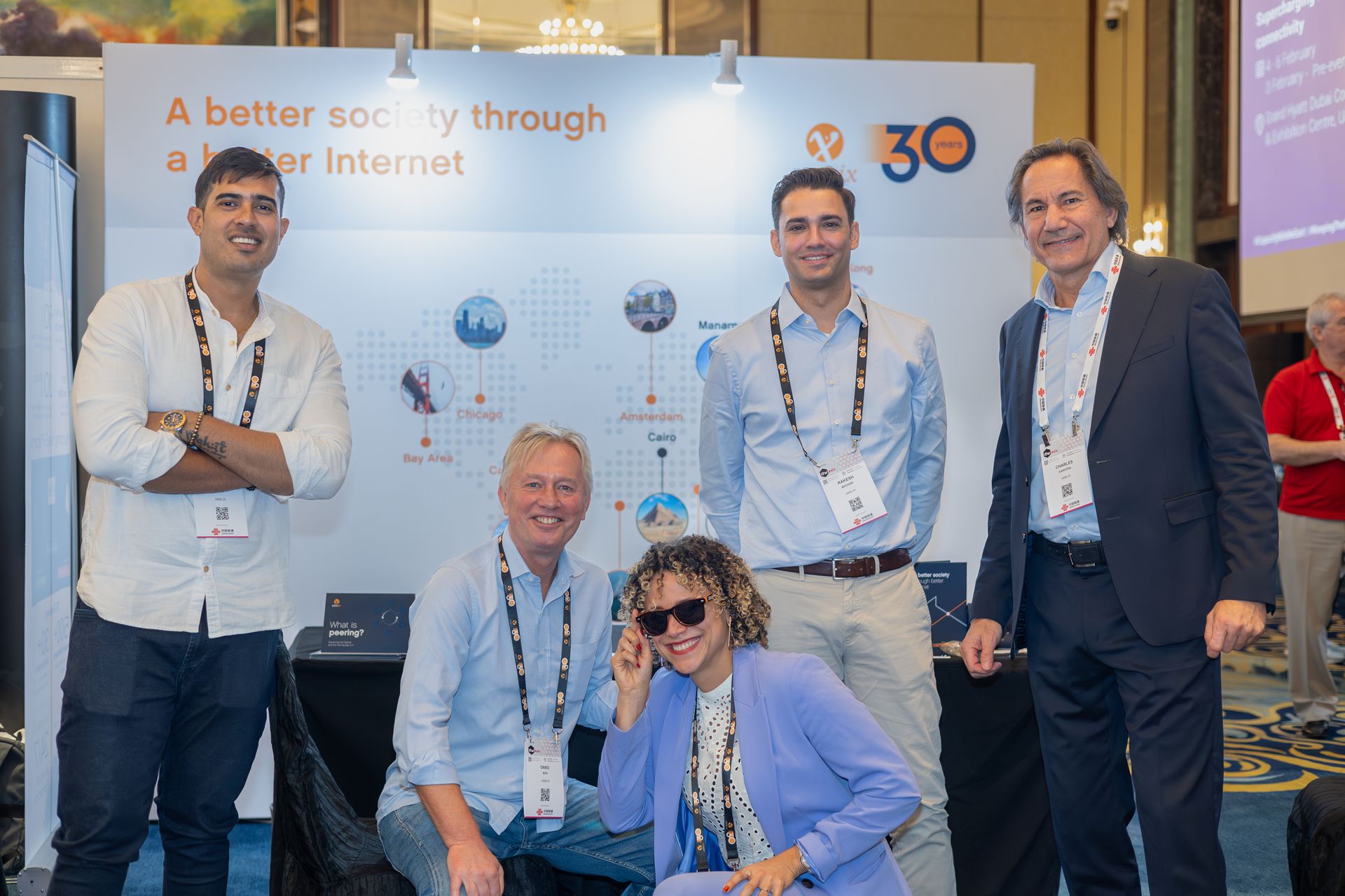 A group of five professionals posing for a picture at an event exhibition stand. The backdrop banner reads 